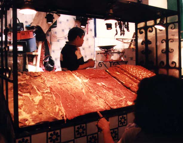 A BBQ vendor with all of the meat selections on display.  Pick the ones you want and then in a short time get a tasty BBQ plate.  Note the fancy lighting to make sure the meats look their best!
